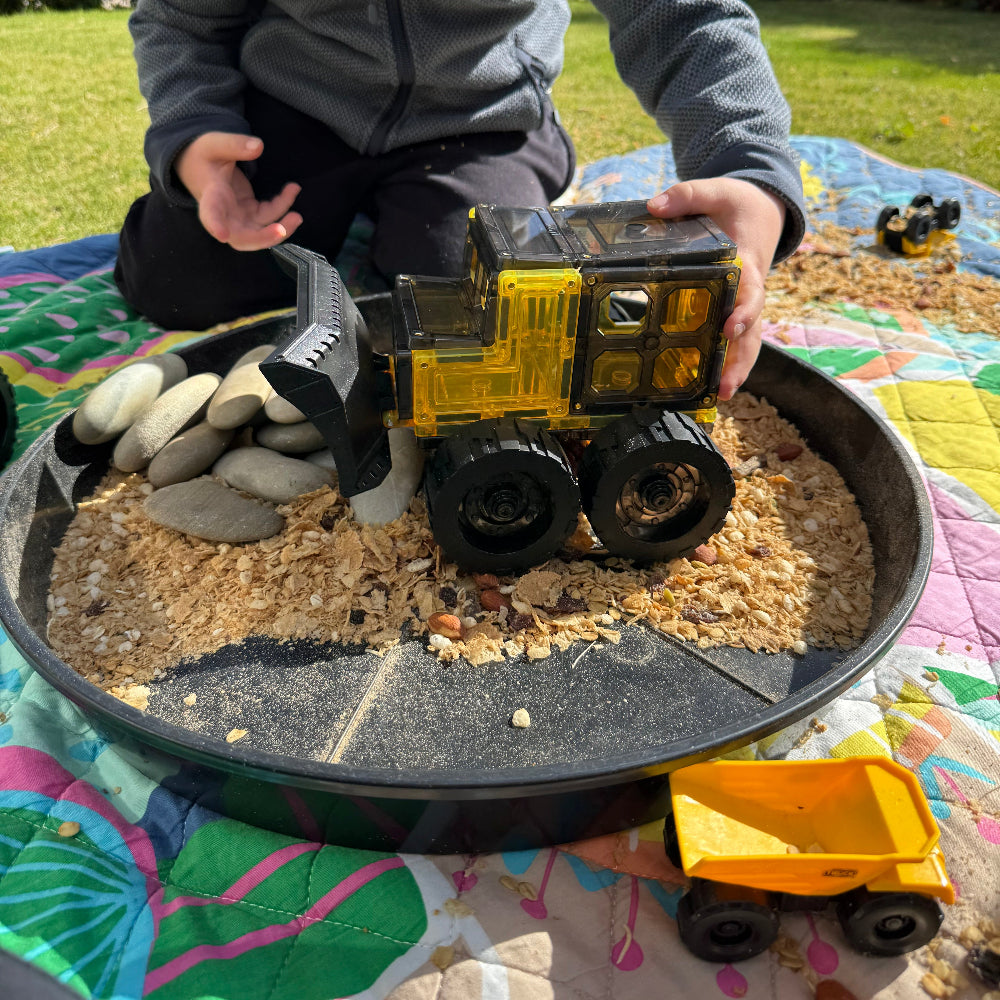 Child playing with magnetic toy digger  a pan filled with sand and stones.