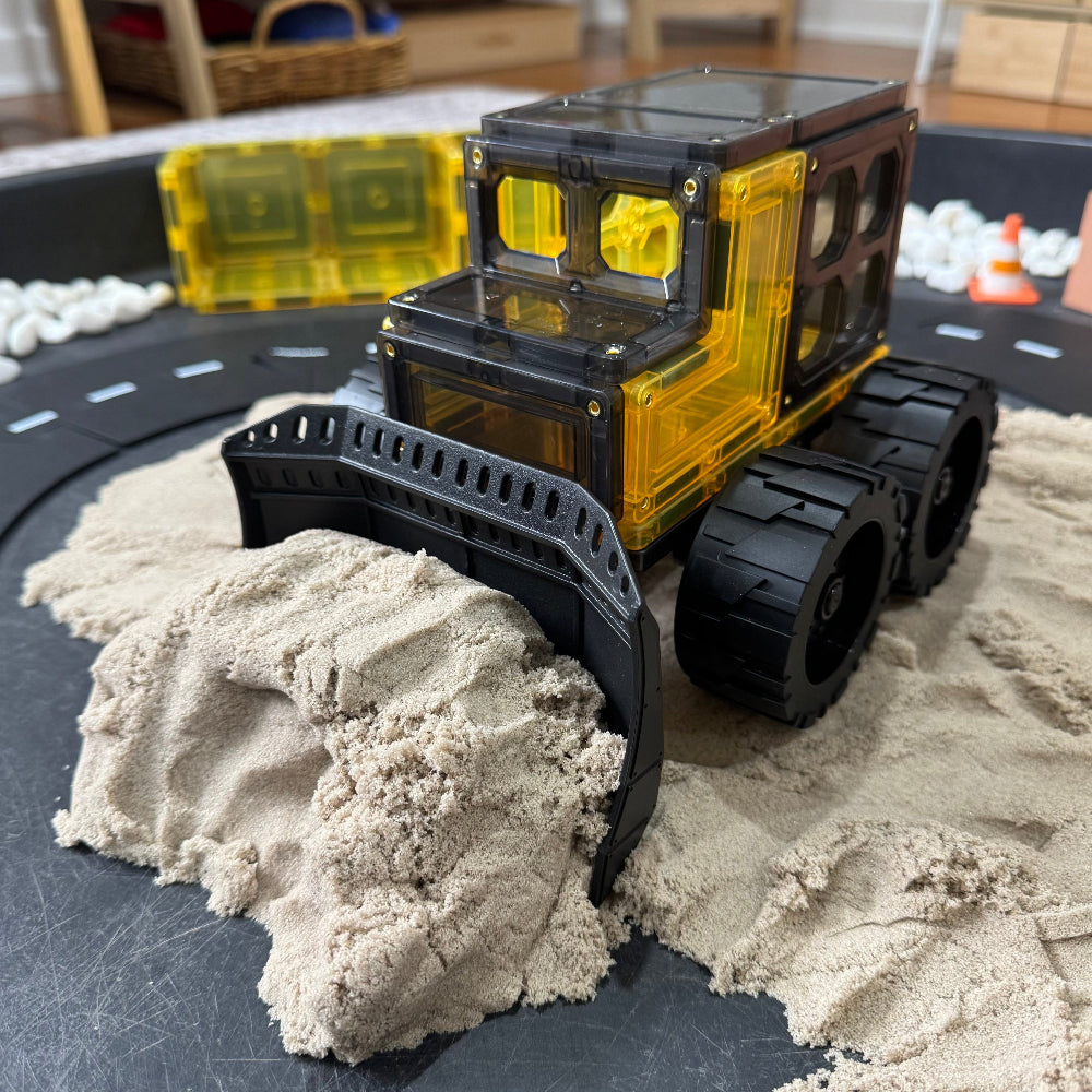 Magnetic tile bulldozer pushing kinetic sand on a tuff tray with a track layout in the background