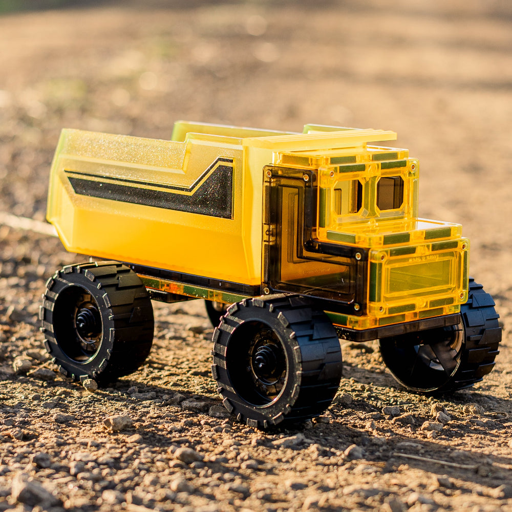 Yellow magnetic tile toy dump truck on gravel road surface