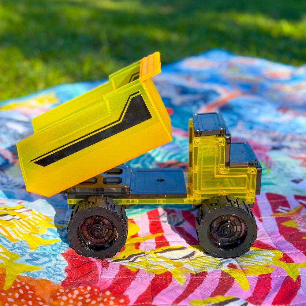 Yellow and black magnetic toy dump truck on a colourful blanket outdoors with grass in background