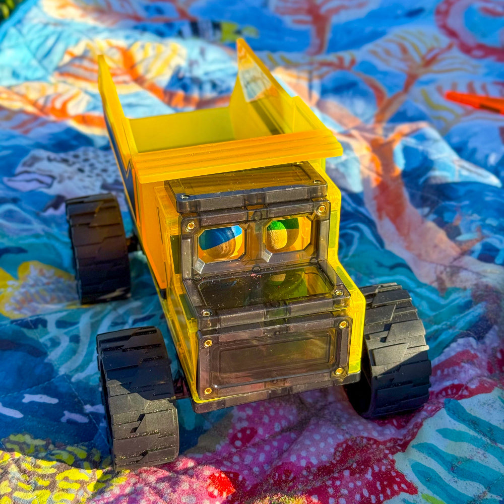 Yellow magnetic toy dump truck on a colourful blanket outdoors