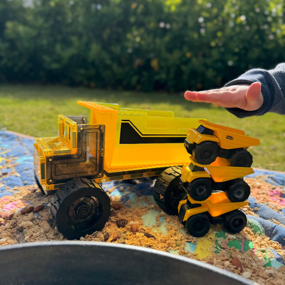 Yellow toy dump truck on a textured surface with 3 small dump trucks and a hand showing the size comparison of the large dump truck