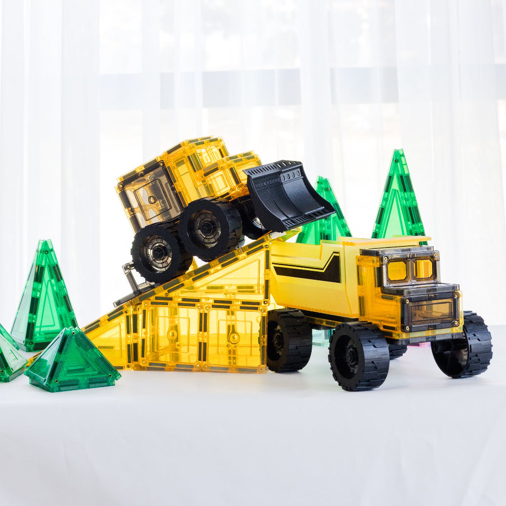 Toy bulldozer on a small ramp with magnetic tile dump truck and green toy trees on a white background