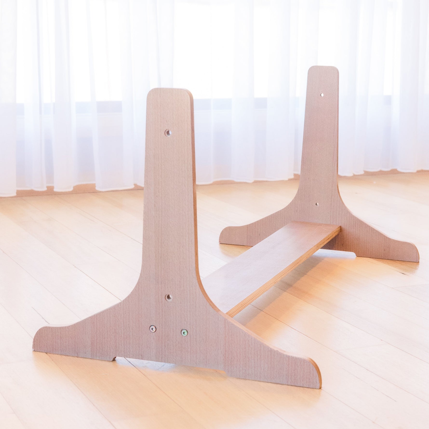 Beech wood stand for multi-board sitting on floor with white curtains in background