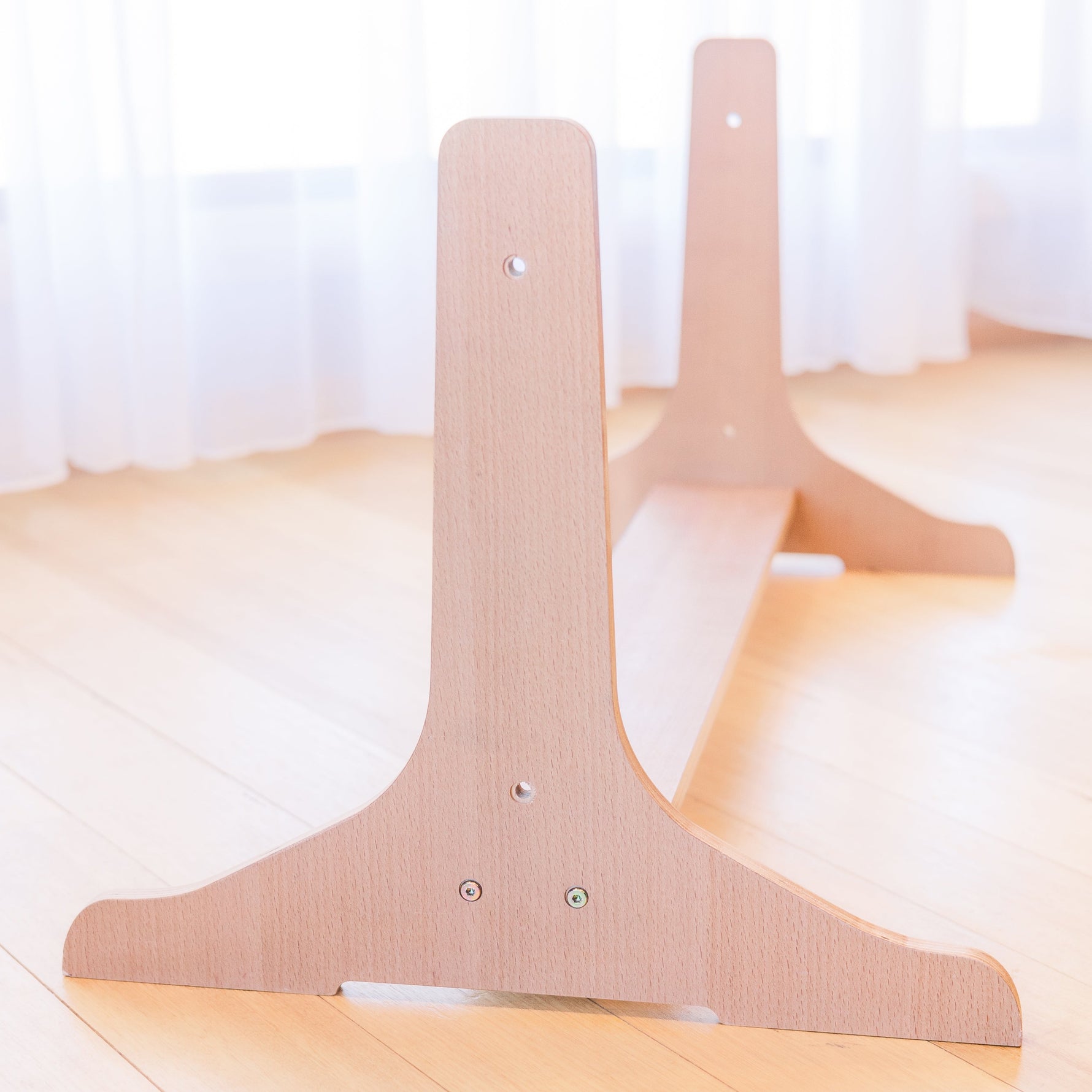 Beech wood stand for multi-board sitting on floor with white curtains in background