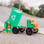 Toy magnetic tile garbage truck with green body and orange details on a road