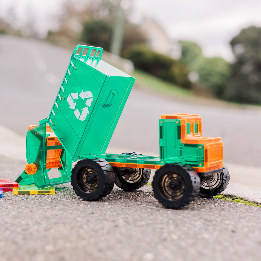 Toy magnetic tile garbage truck with green body and orange details on a road