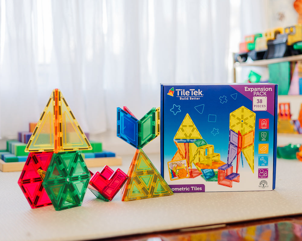 Colourful geometric tiles and Tile Tek expansion pack on a table with a white curtain background