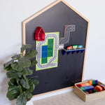 Learn & Grow Toys Multi-Board with blackboard stuck to wall with train and road toppers on the board with ficus leave plant on floor