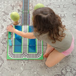 Child playing with magnetic tile train toppers with magnetic tiles and wooden trees on floor