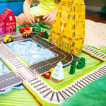 Child playing with train and road toppers and wooden trees and cars and trains with sarahs silk on bottom 