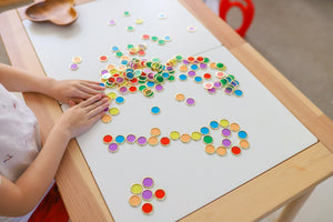 Metal Rimmed Counting Chips for counting, sensory and creative play displayed across white desk with child playing